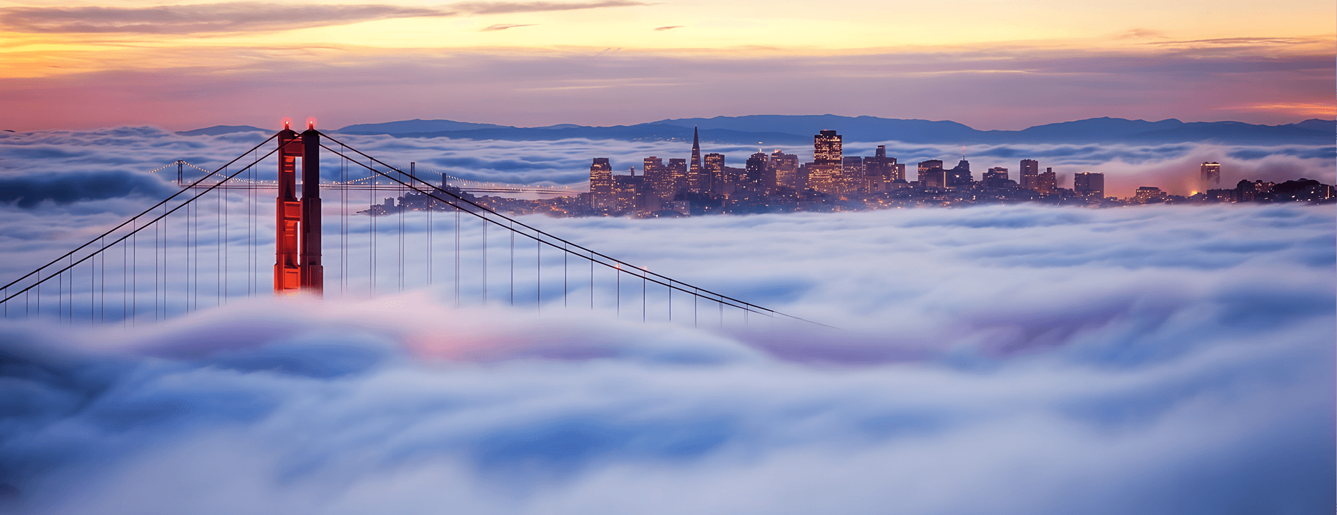 Golden Gate Bridge and the San Francisco skyline above a bank of fog at sunset